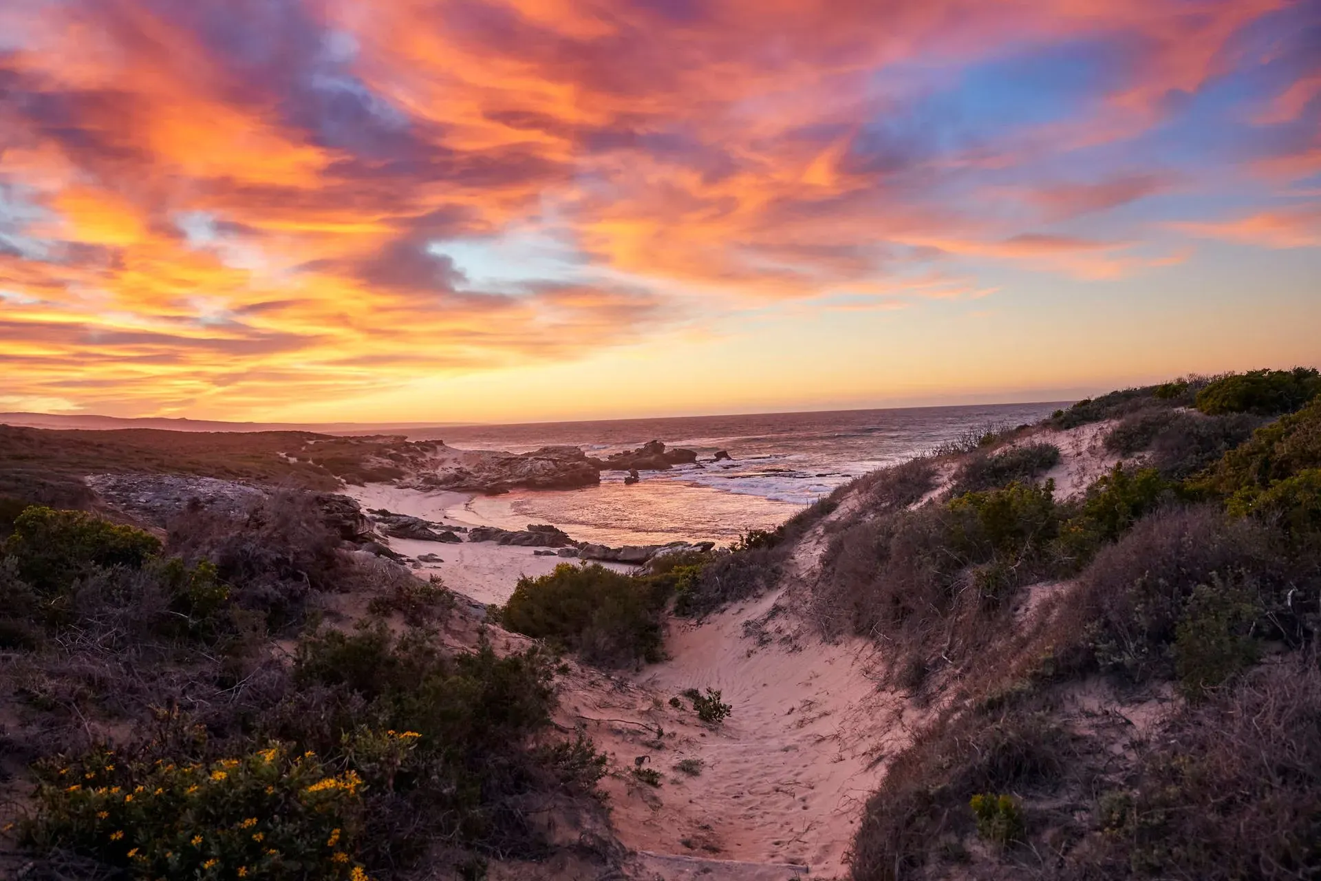 A stunning sunset casts vibrant colors over the ocean and sand dunes at a South Africa beach resort.